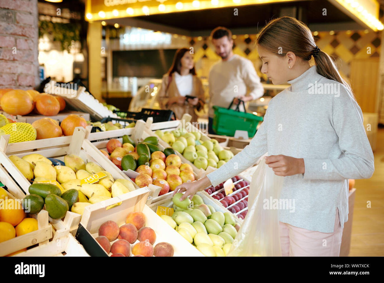 Pretty casual girl taking green apple from display before putting it into packet Stock Photo