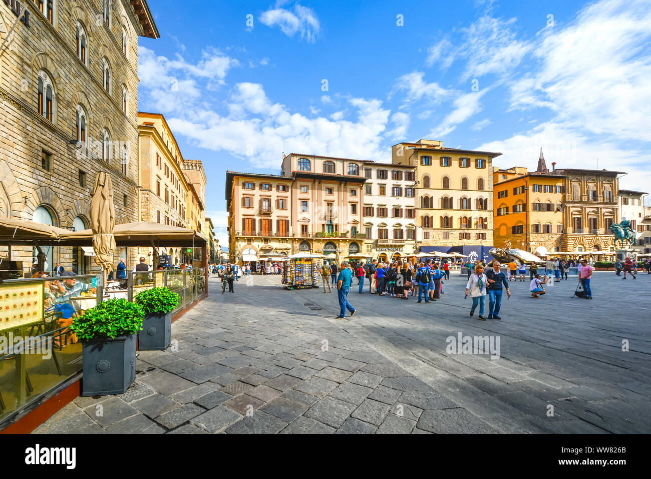 Tourists enjoy the warm afternoon at Piazza della Signoria in Florence Italy as they dine at an outdoor cafe and buy souvenirs from a gift stand Stock Photo