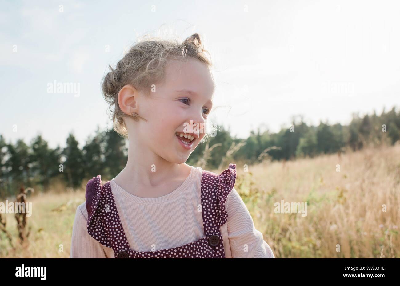 portrait of a young girl smiling walking through a meadow at sunset Stock Photo