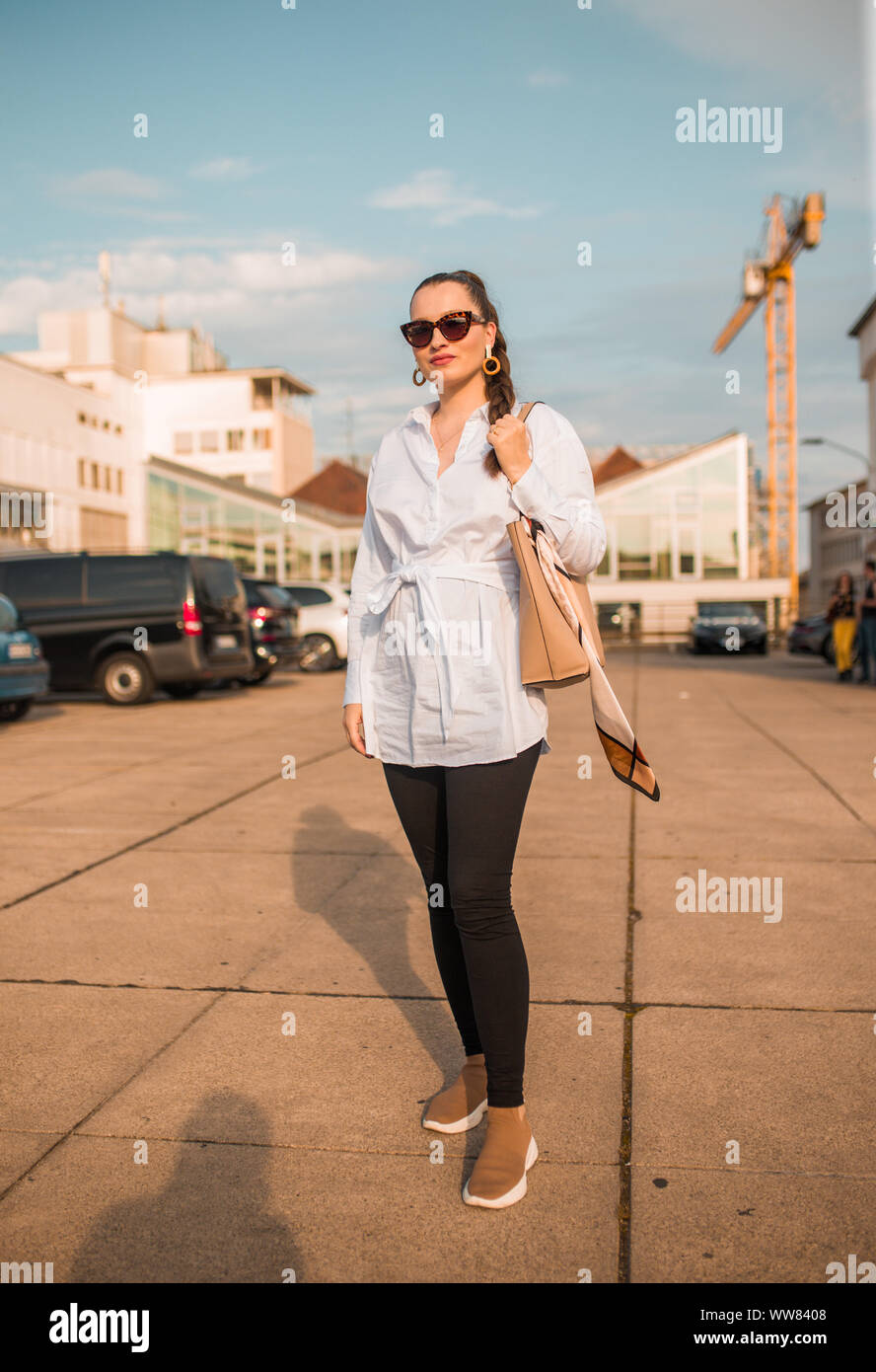Portrait of young woman standing on sidewalk and holding bag Stock Photo