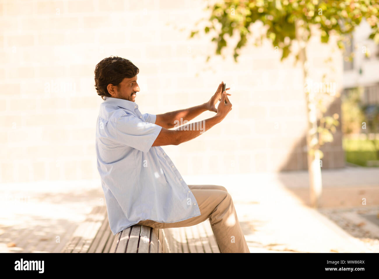 young with smart phone sitting on a bench outside Stock Photo