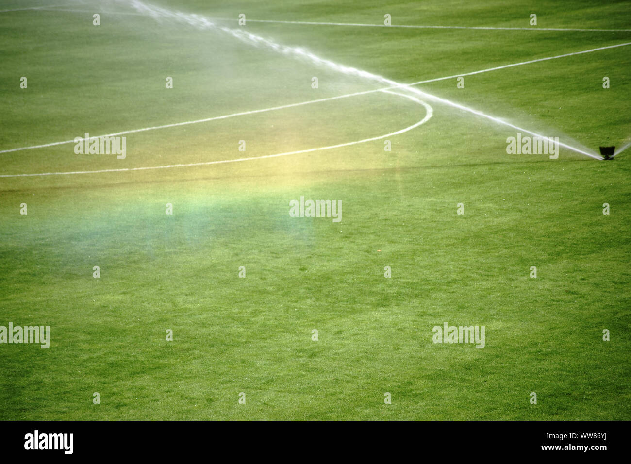 The green lawn of a football field with an irrigation system making a rainbow Stock Photo