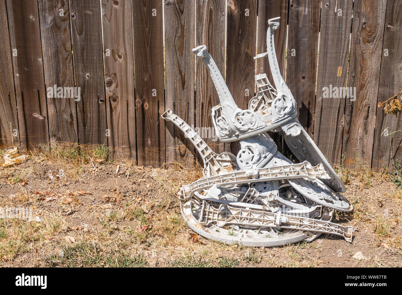 Two plastic lawn chairs and a matching table that have been destroyed are stacked in a pile waiting to be recycled in someone's front yard. Stock Photo