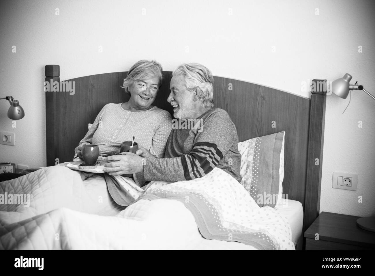 caucasian aged couple doing breakfast at home in the bed, nice natural scene at home for togetherness life concept, love and carefree people married, laughing together starting the day in the morning Stock Photo