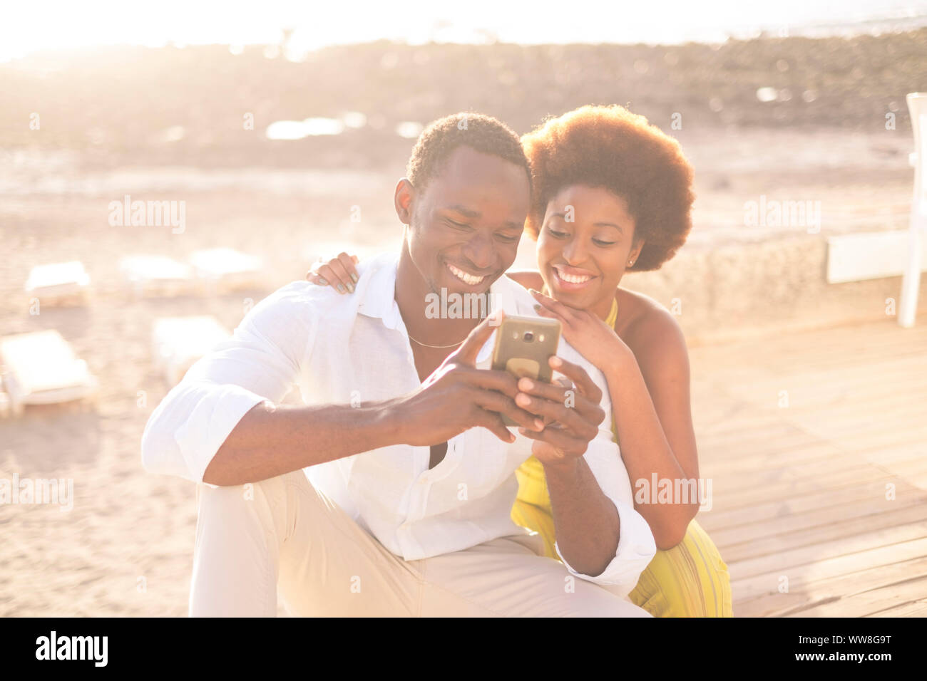young happy couple afro American afro race multi-ethnic racial diversity enjoy phone and internet in outdoor leisure activity during the bright and golden sunset with light in background, smile and stay together Stock Photo