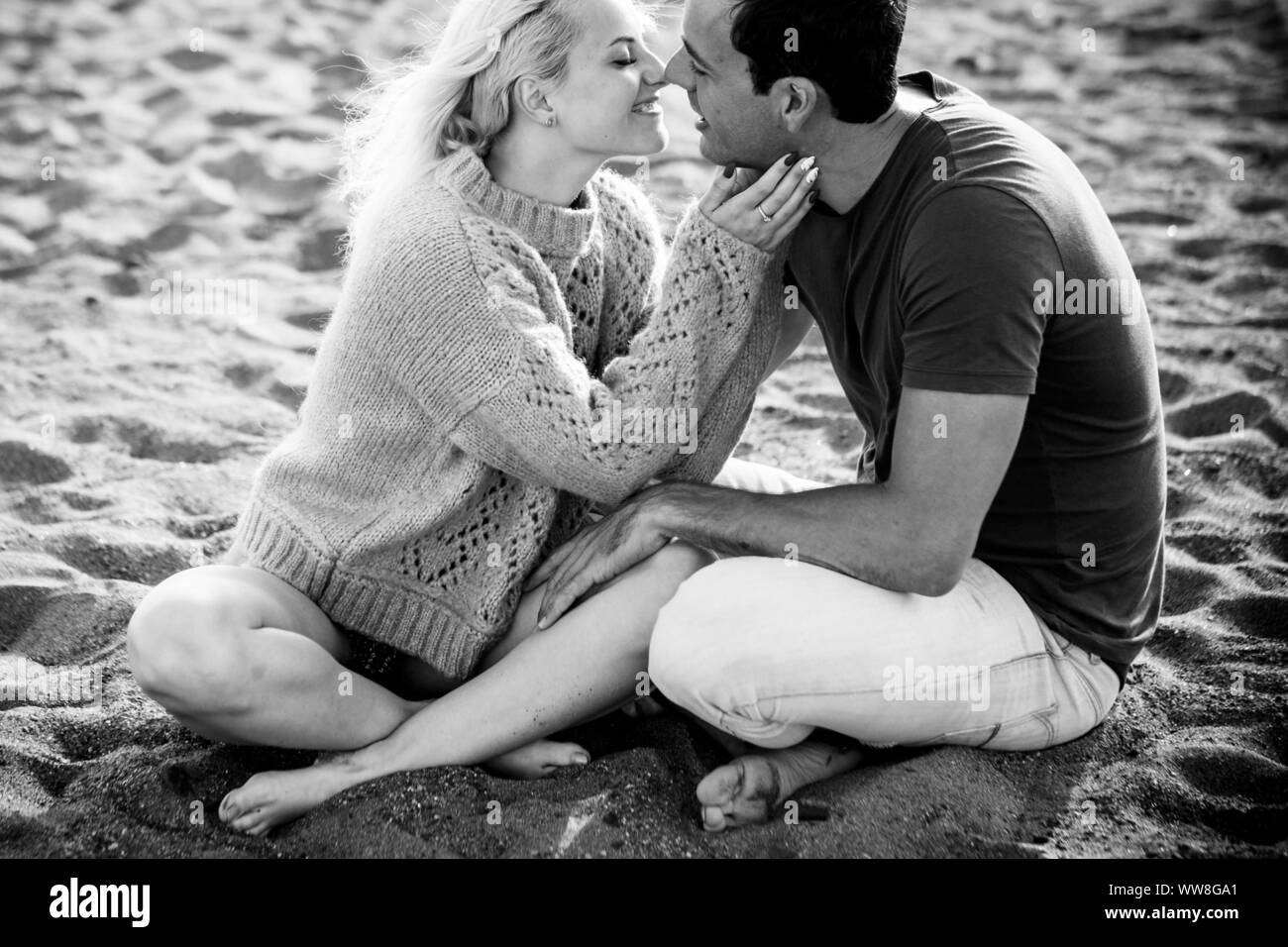 beautiful model couple caucasian young lady and man stay in love hugging and sitting on the beach, blonde and black hair in relationship outdoor leisure activity, love and youthful attractive people Stock Photo
