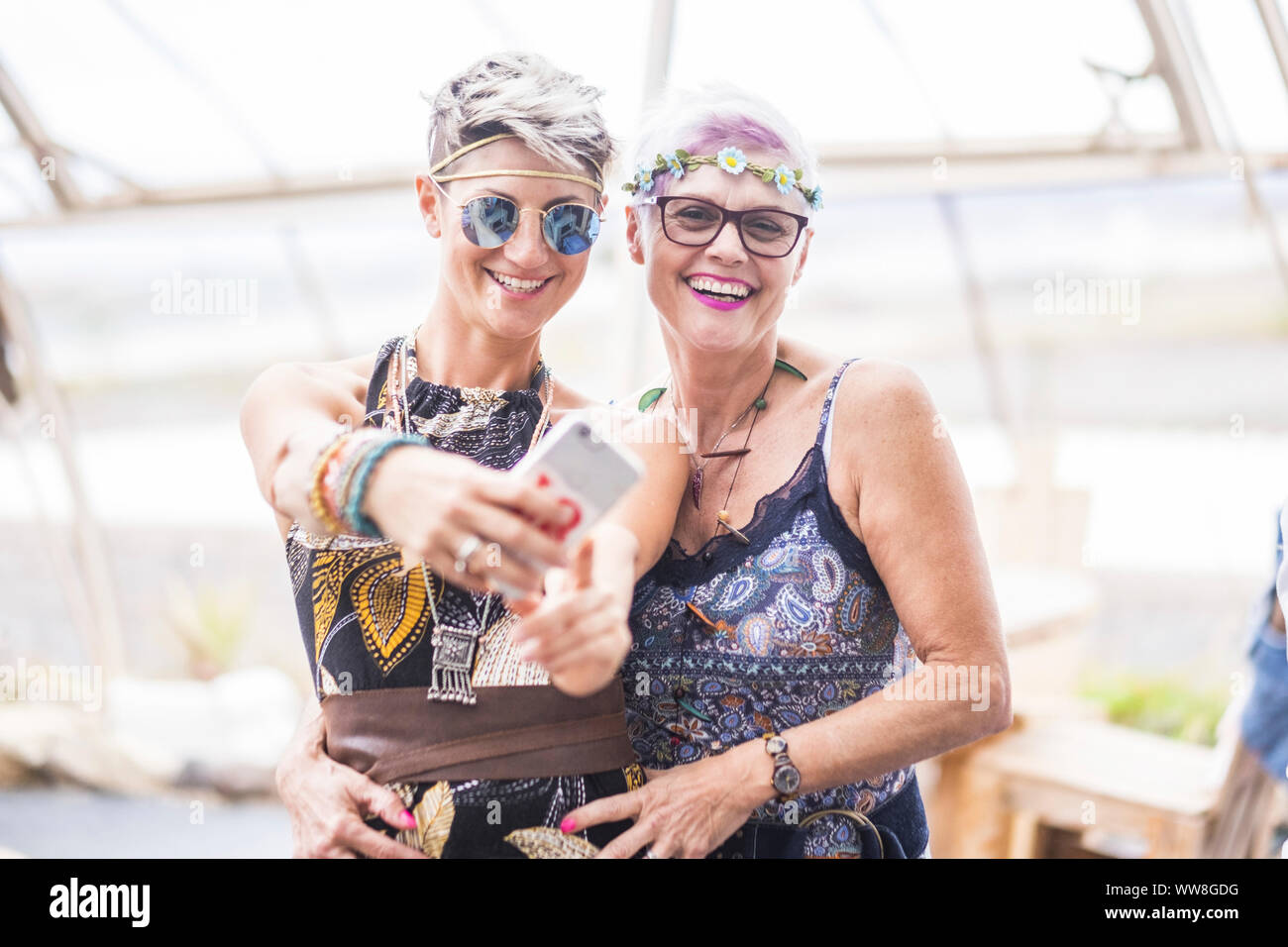 hippy couple of caucasian beautiful females use a smart phone, Different ages nice attractive people stay together in happy leisure activity with friendship, Sharing content on social for cheerful old and young ladies Stock Photo