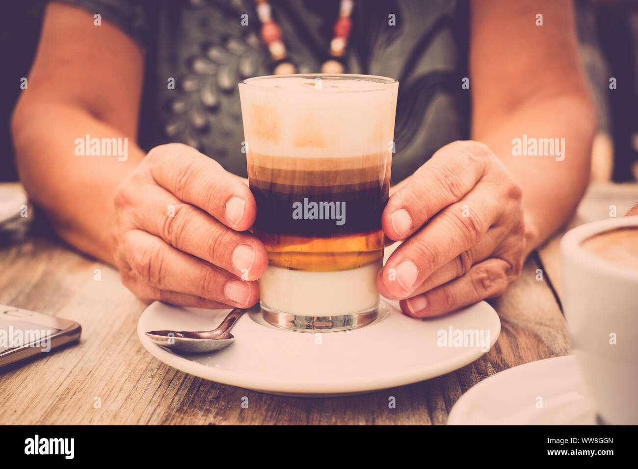 Close-up of hands with transparent glass of coffee and wooden table Stock Photo