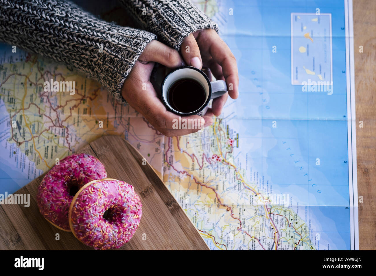 Planning the next vacation destination travel during the breakfast morning to start a new wonderful day, coffee and a pair of sweet donuts on a world map, hands taking the cafe and looking the places to discover Stock Photo