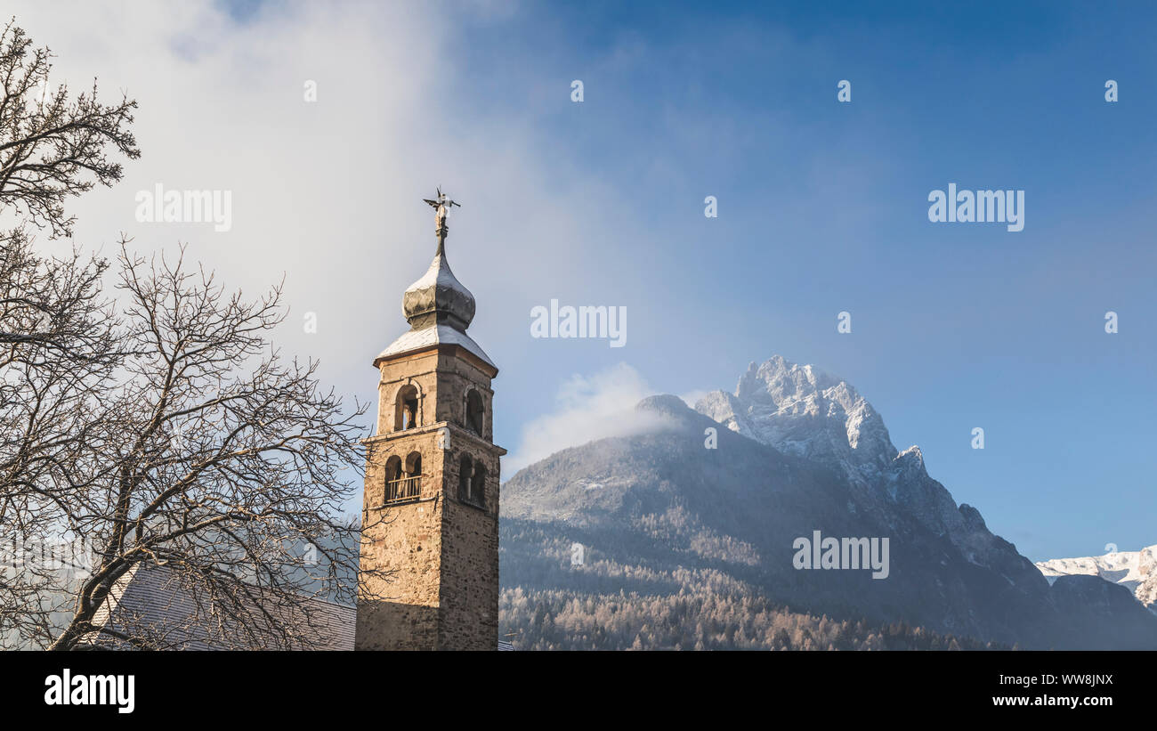 The bell tower of the ancient church of San Cipriano (St. Cyprian) in Taibon Agordino, on the background the Agner mountain, Belluno, Veneto, Italy Stock Photo