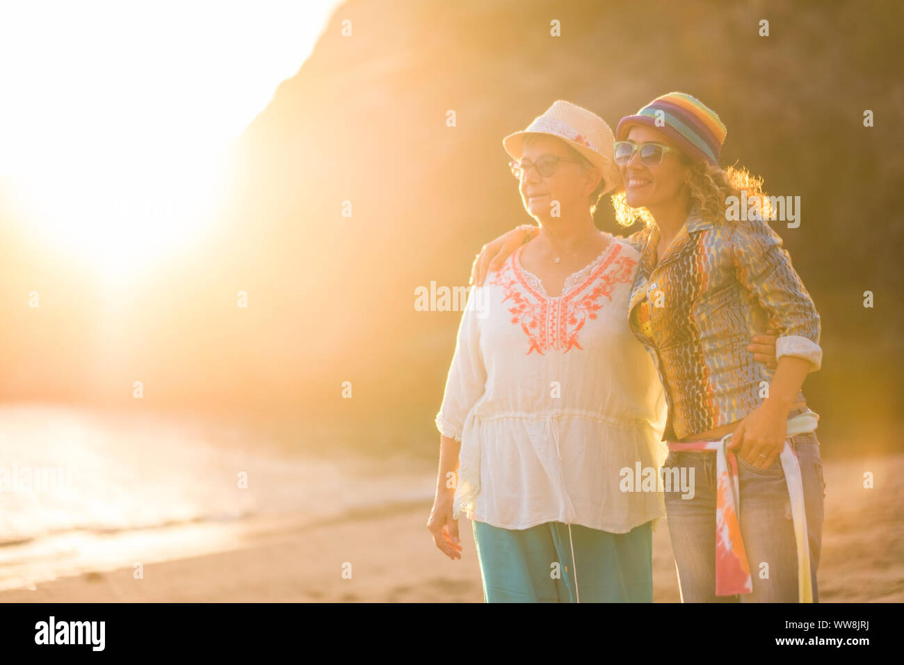 couple of friends females outdoor at the beach during a beautiful sunset with golden light. ocean and shore in background for vacation concept iand relationship with young and woman people Stock Photo