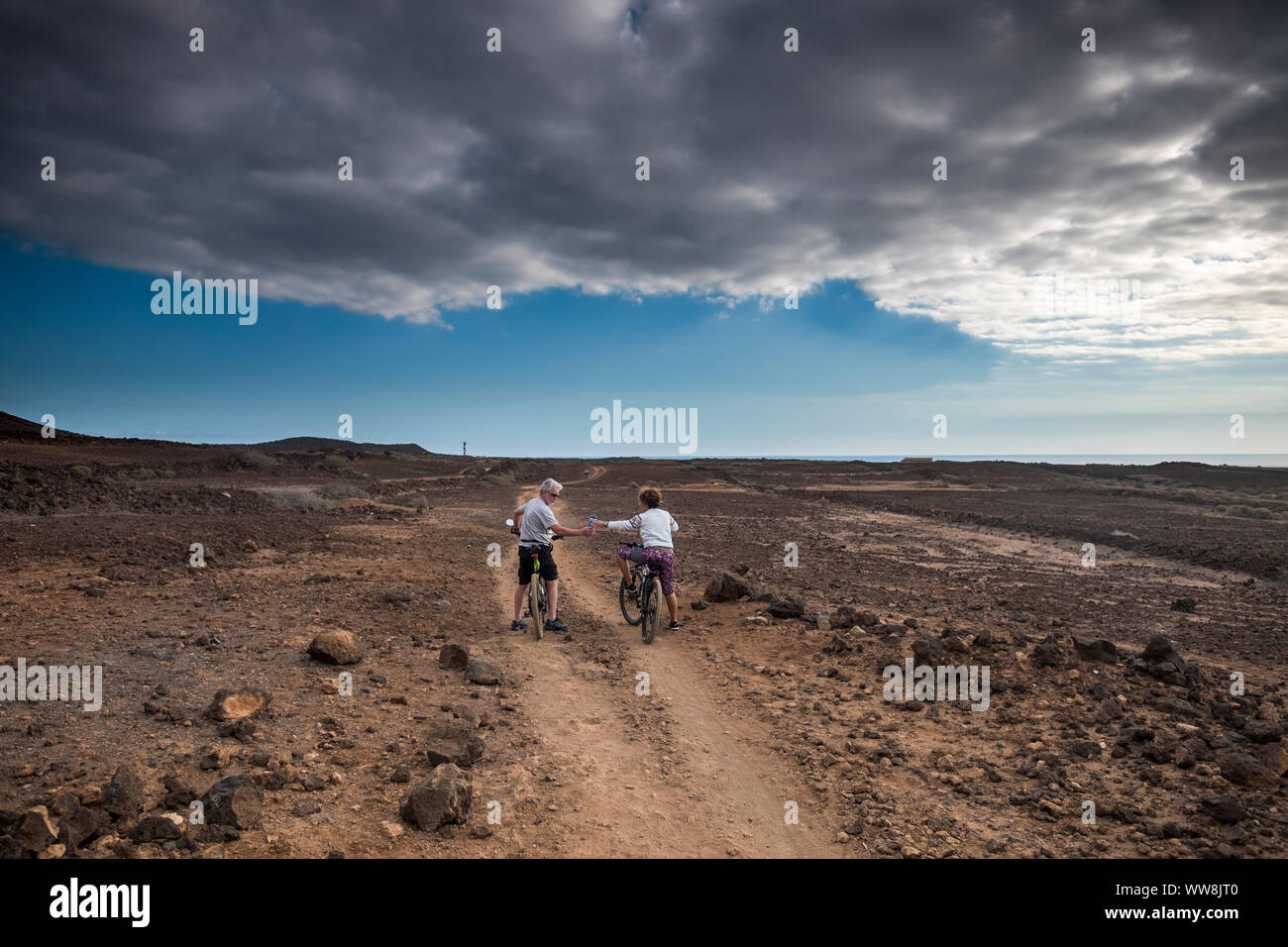 couple of rider with mountain bike follow a path in the middle of an ardi desert. vacation and discover adventure in leisure sport activity for caucasian people enjoy the day Stock Photo