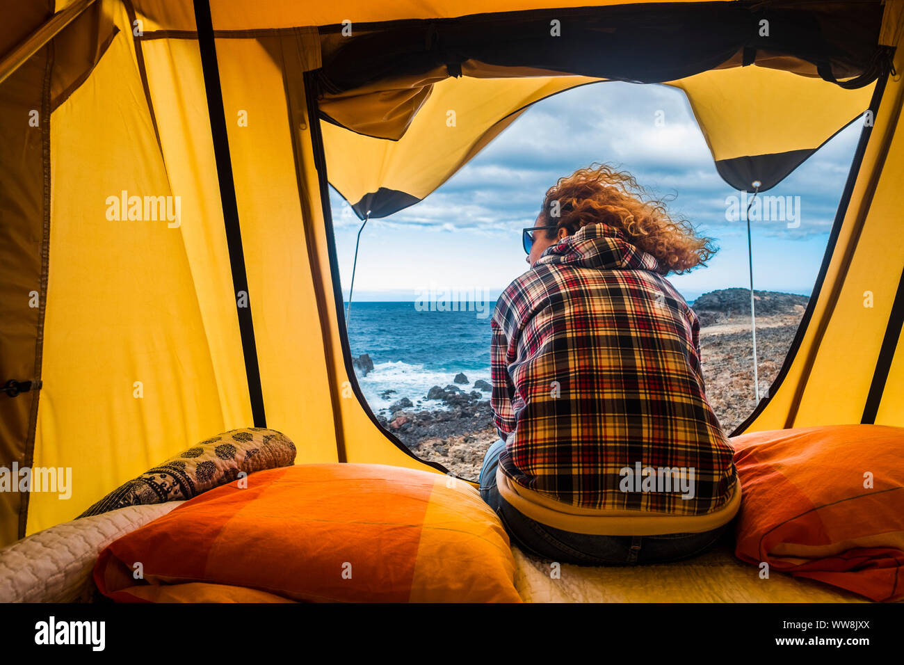 nice woman view from backside sitting outside of a tent mounted on a car. outdoor freedom vacation alternative concept looking ocean out of the door. feeling sea and adventure Stock Photo