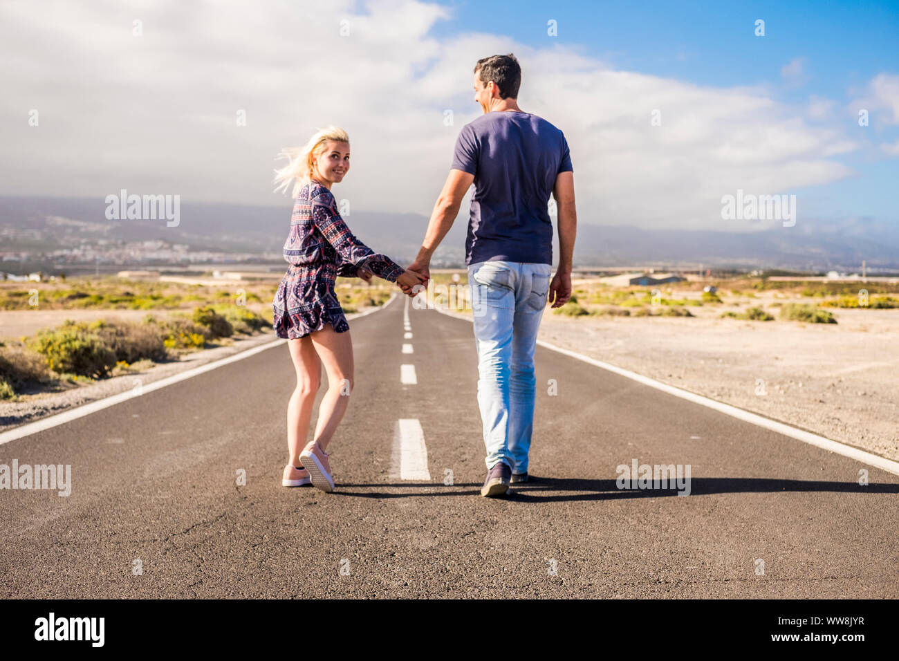 nice caucasian couple in relationship taking hands and walk together on a long way road straight to the future. life forever in coule and family in love concept. beautiful landscape and desert place Stock Photo