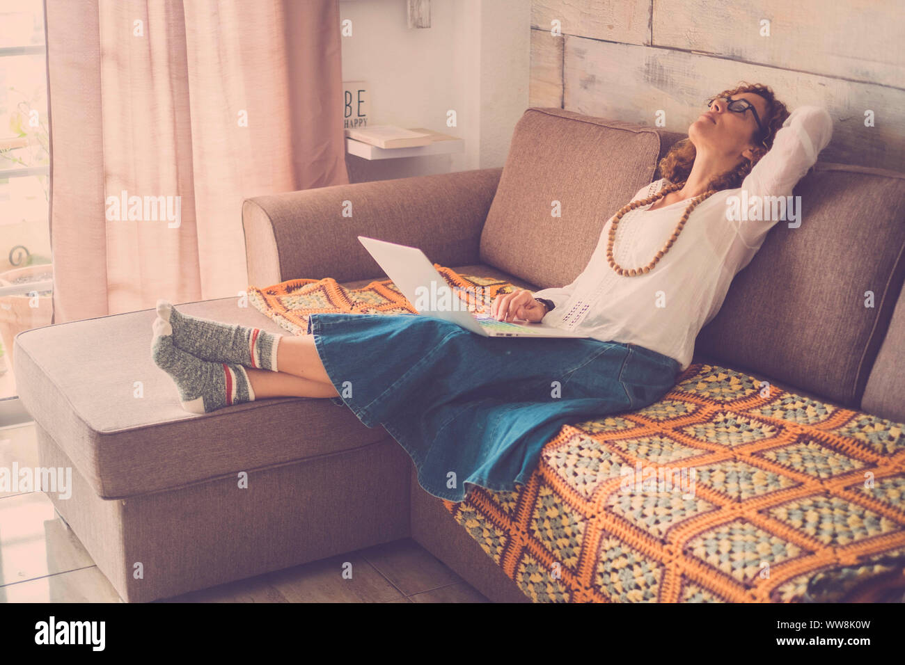 stressed out beautiful middle age woman working at laptop on the sofa at home. internet alternative office for online digital worker. tired looking on the top, wearing funny socks Stock Photo