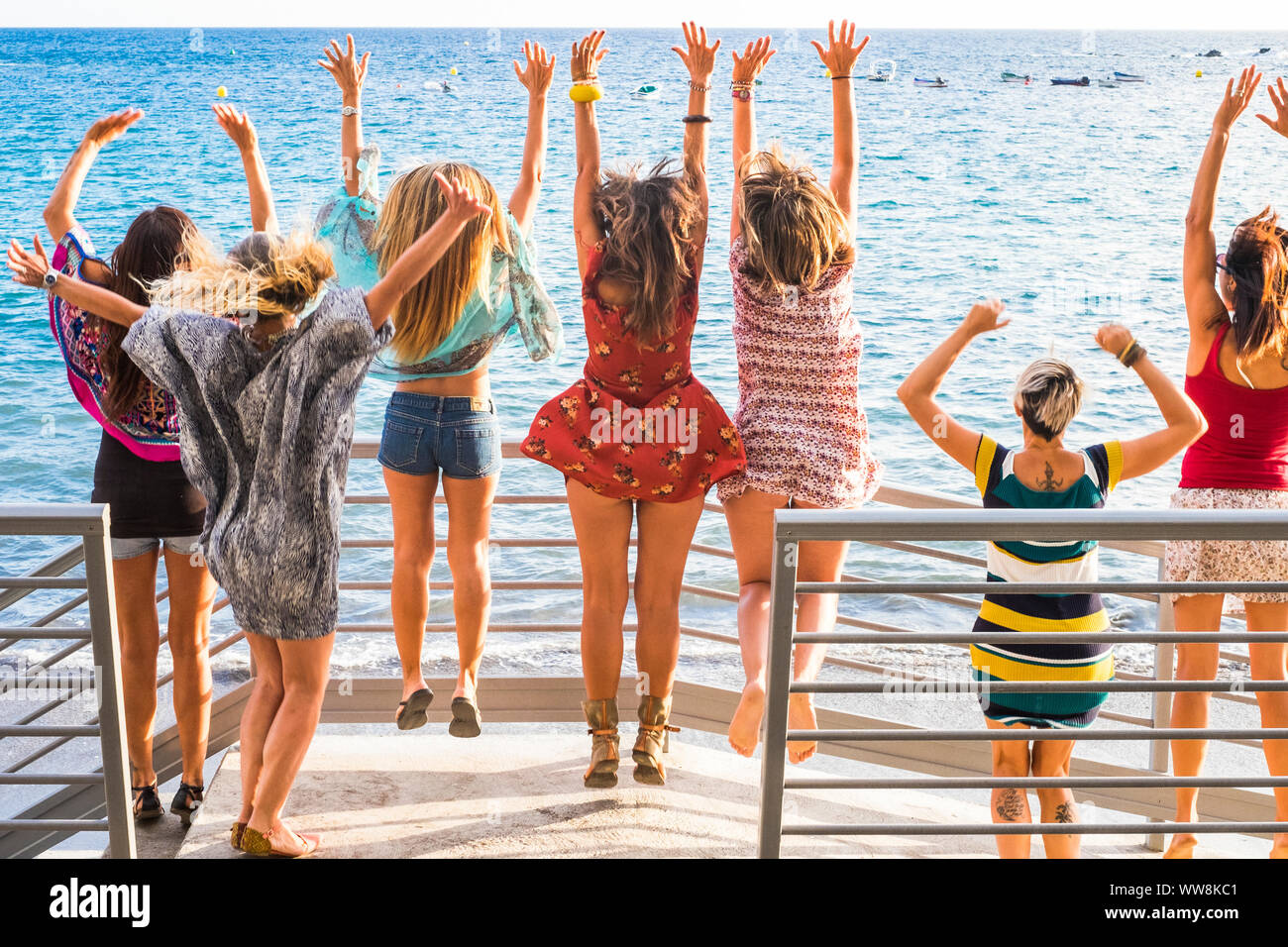 group of women enjoying and celebrate summer vacation all together saying hallo to the ocean and the nature. young people leisure activity, all hands up and vintage colors style. fashion dresses view from backside Stock Photo
