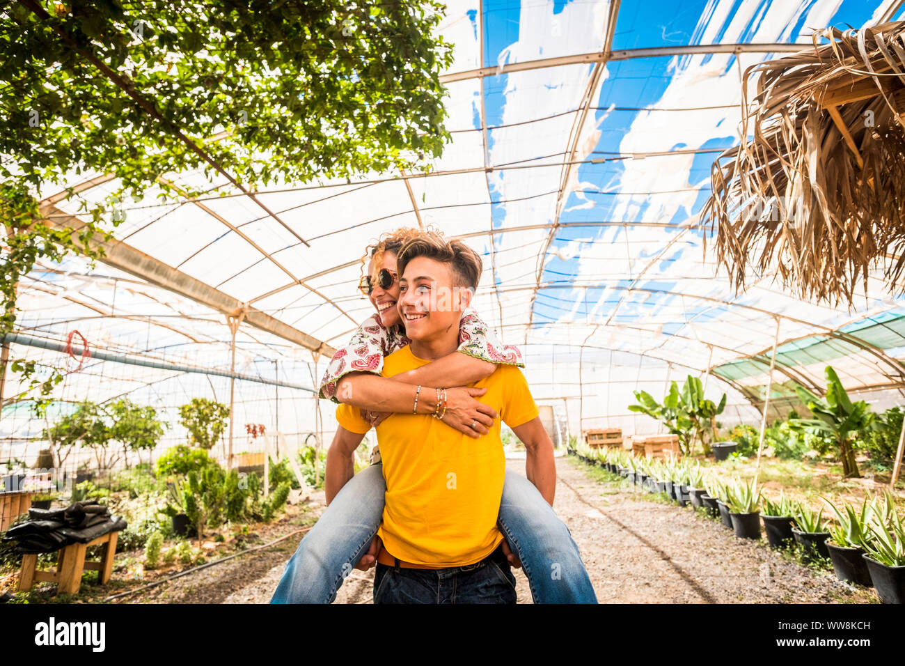 young beautiful teenager play with his mother middle age pretty woman carrying her to his back. couple mother son having fun together like a perfect family in outdoor leisure activity. happy people concept Stock Photo
