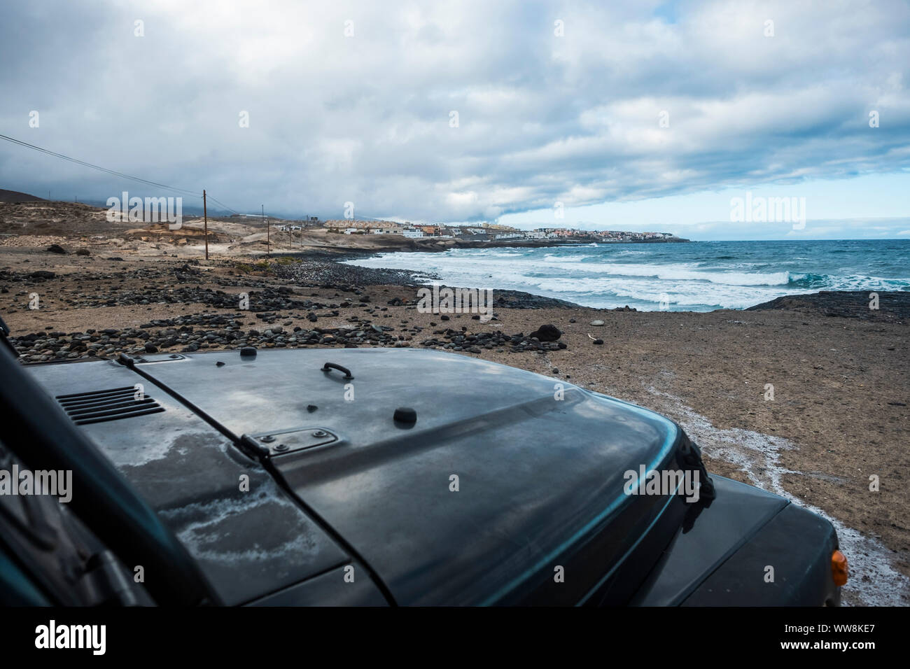 car parked near the coast in vacation day. blue colors background viewing ocean and waves. black vehicle parking and enjoying the adventure Stock Photo