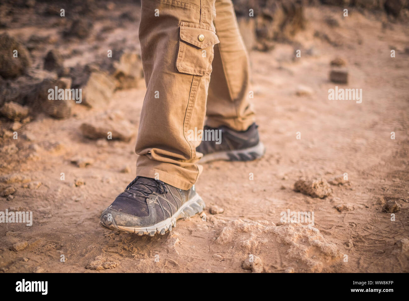 closeup of shoes do trekking on the ground in desertic arid place. man freedom concept and dirty of sand wear. exploring and discover alternative vacation and places around the world Stock Photo