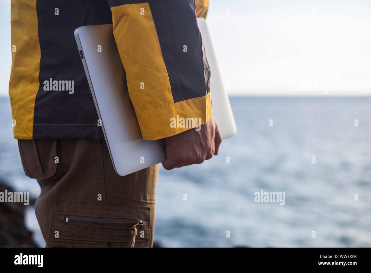 close up of man's hand bringing a laptop in front of the ocean. travel and work related adventure and independent lifestyle far away from the stress of an usual work at the city. modern opportunity with internet Stock Photo