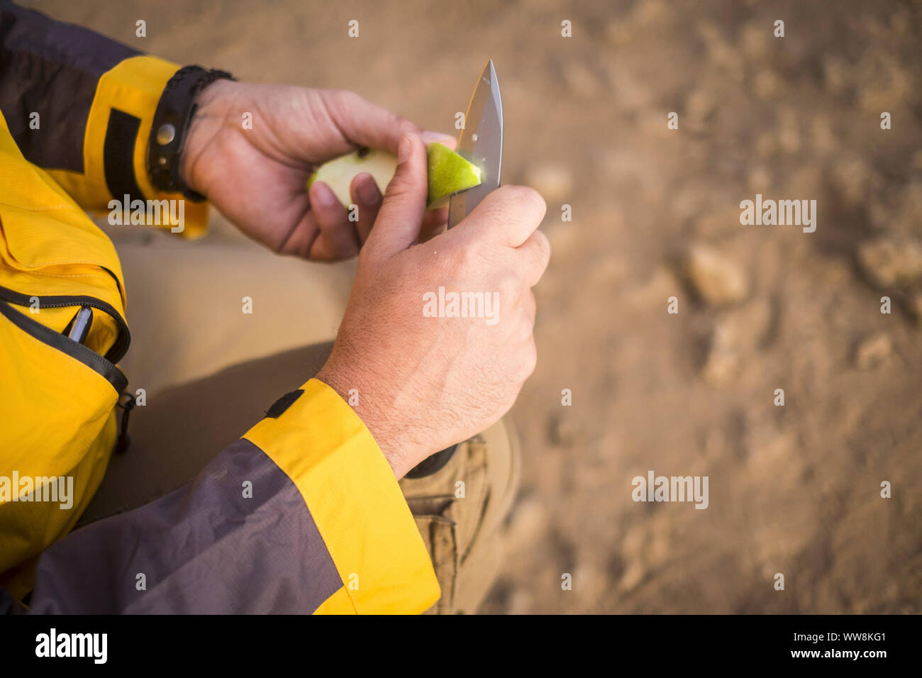 close up of human hands cutting a green apple with a knife outdoor during an adventure trekking outdoor in the desert. exploring the world and get an alternative travel and vacation concept Stock Photo