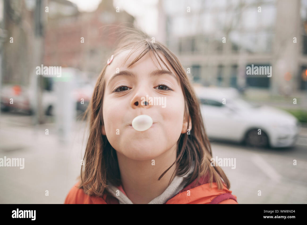 little girl chewing gum doing a pink bubble looking to the camera Stock Photo