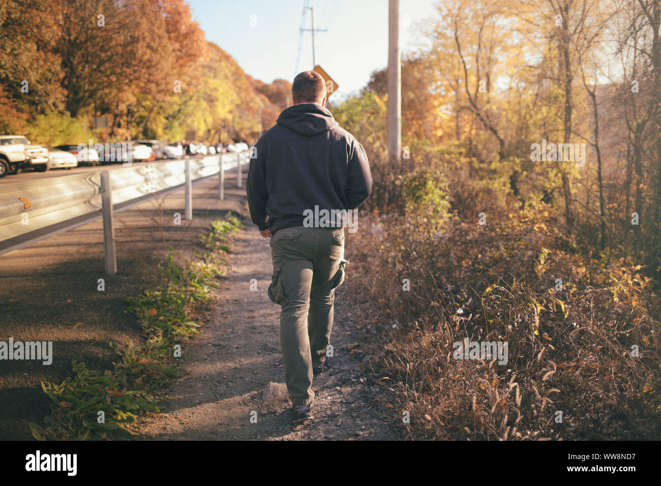 blonde young man walking on the side of a road in upstate new york Stock Photo