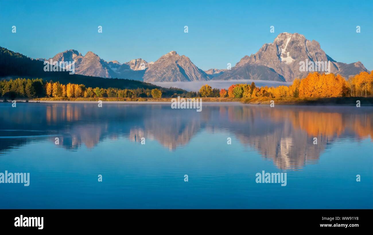 A beautiful early morning landscape scene at Oxbow Bend in the Snake River, with Mount Moran and autumn tree color reflected in the smooth water. Gran Stock Photo