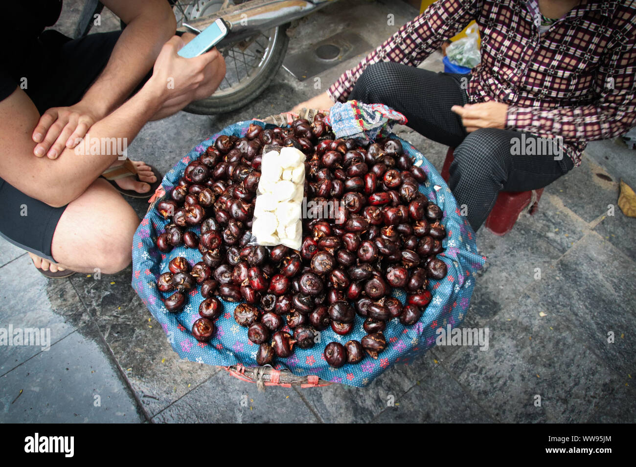 Overhead view of a tourist buying water chestnuts or eleocharis dulcis from a Vietnamese streetfood vendor Stock Photo