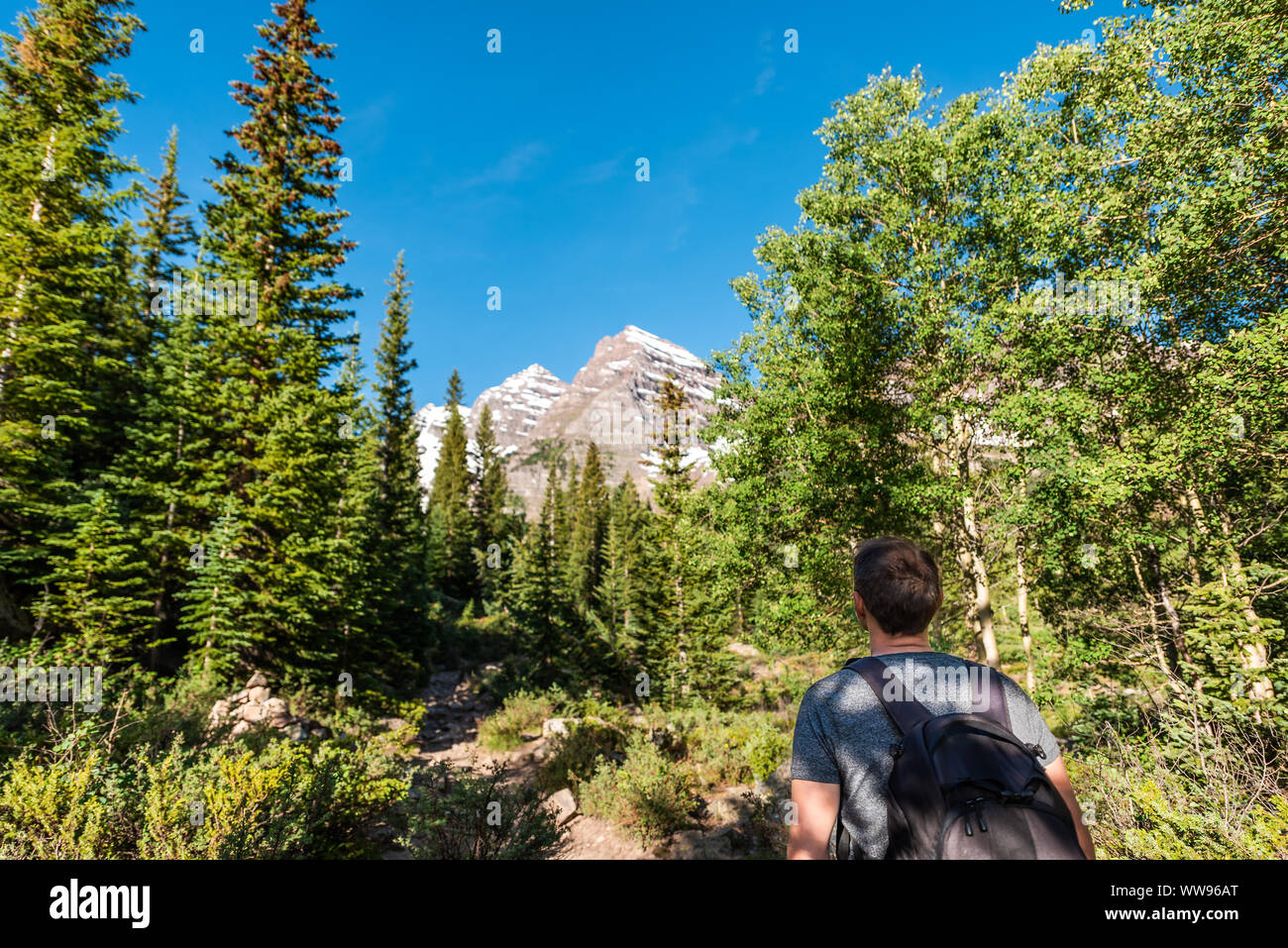 Maroon Bells peak view in Aspen, Colorado with tourist man backpack hiker looking in July 2019 summer on trail path road wide angle view Stock Photo