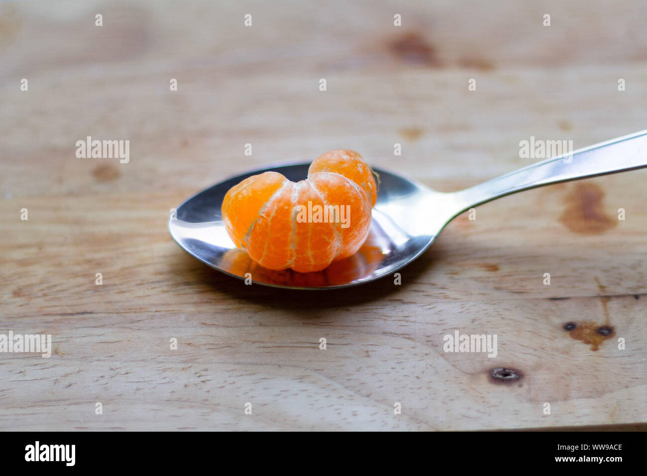 Peeled clementine orange on a spoon showing concept of summer, clean living, wellness and well-being Stock Photo