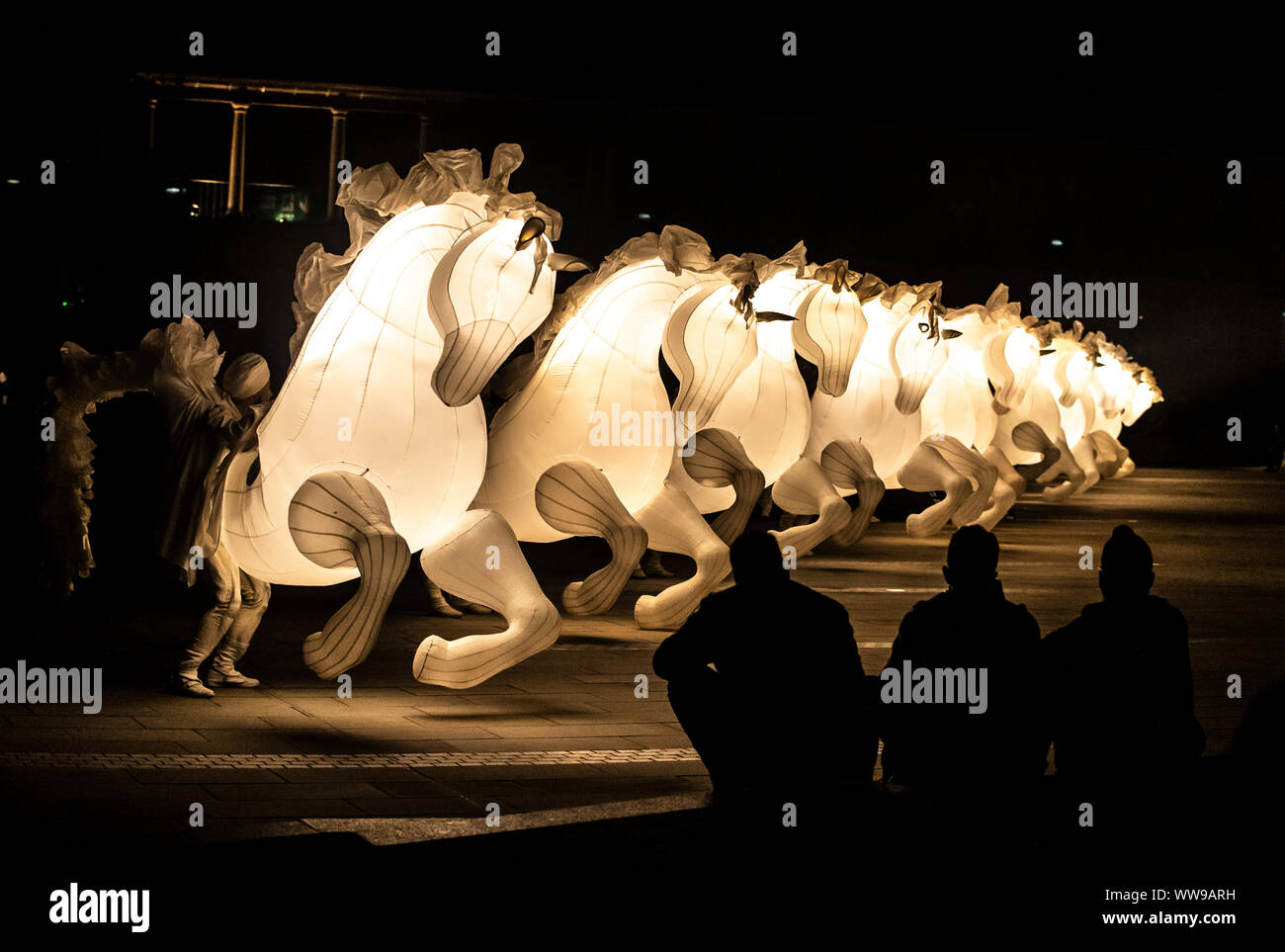 Inflatable glowing white horses perform during arts production FierS a Cheval at the Grade I listed Piece Hall, in Halifax, Yorkshire. Stock Photo