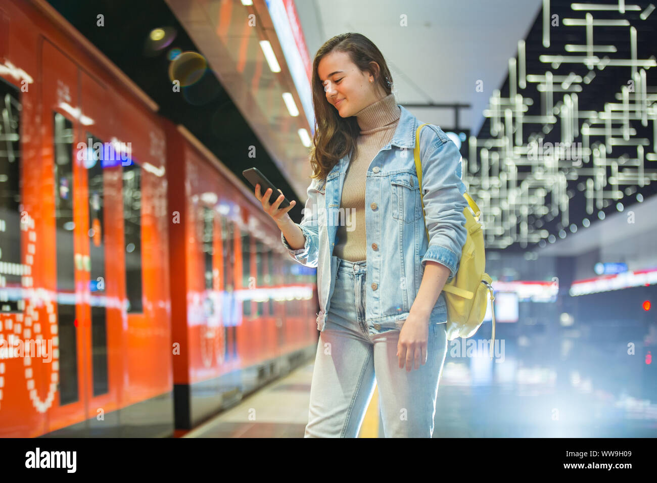 Teenager girl in jeans with backpack standing on metro station holding ...