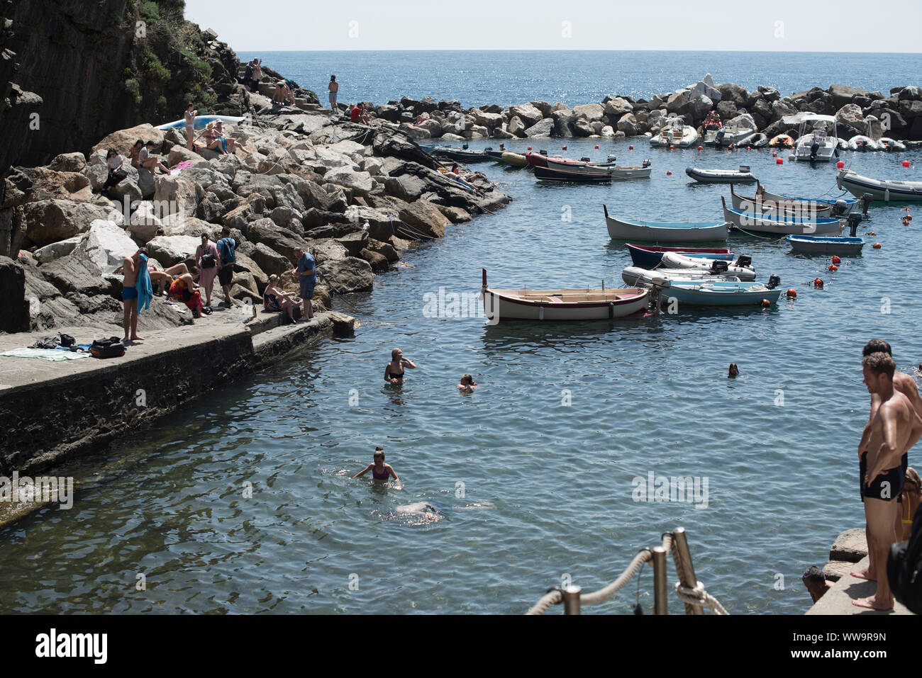 Riomaggiore, Italy - July 2, 2018: On a hot mid-summer day, bathers swim among the boats moored in Riomaggiore, one of the five traditional fishing vi Stock Photo