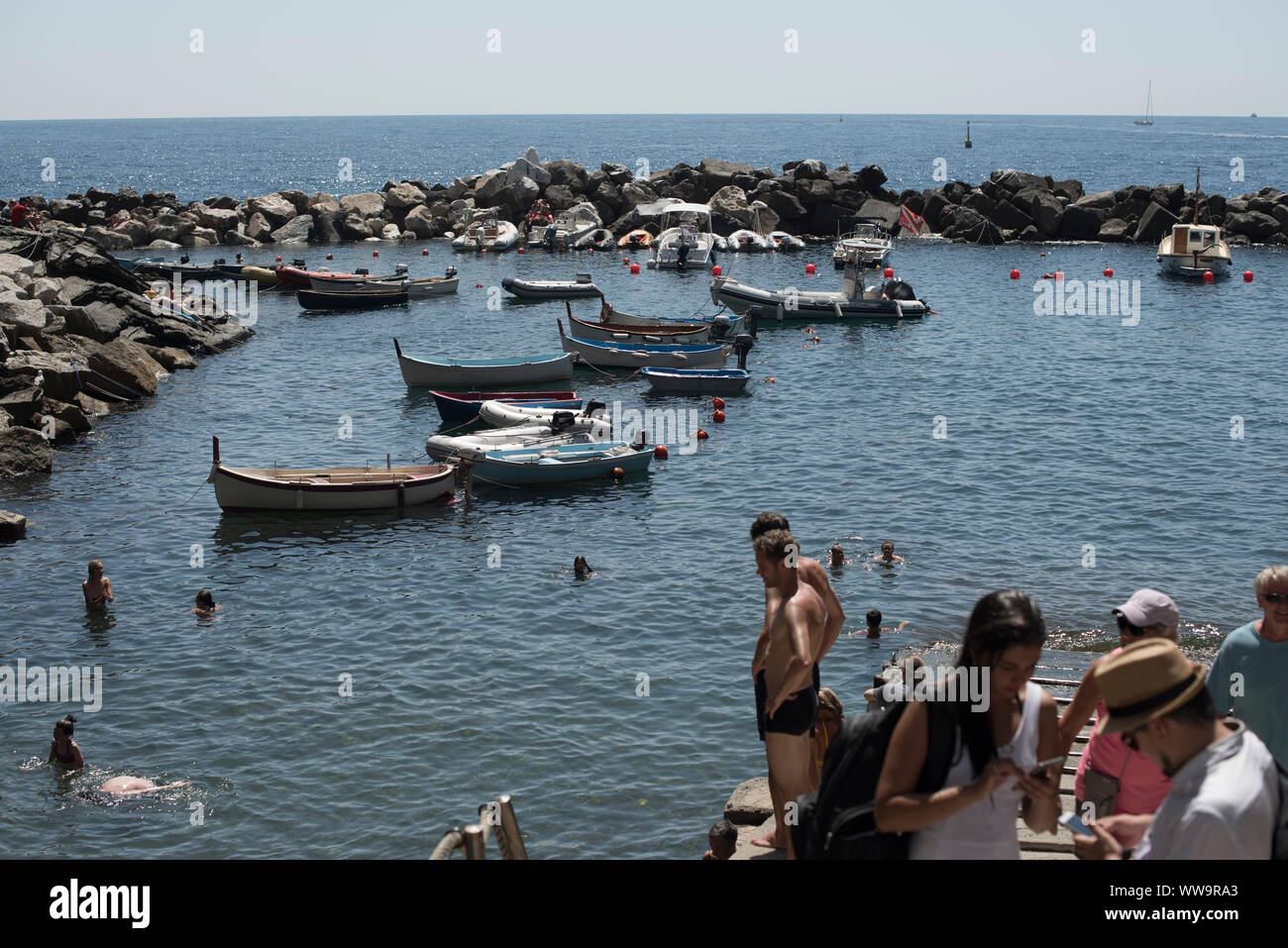 Riomaggiore, Italy - July 2, 2018: On a hot mid-summer day, bathers swim among the boats moored in Riomaggiore, one of the five traditional fishing vi Stock Photo