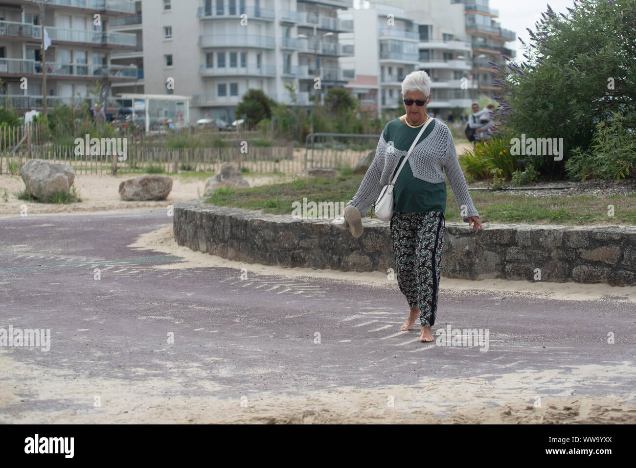 An elderly woman walks barefoot to the beach Stock Photo Alamy