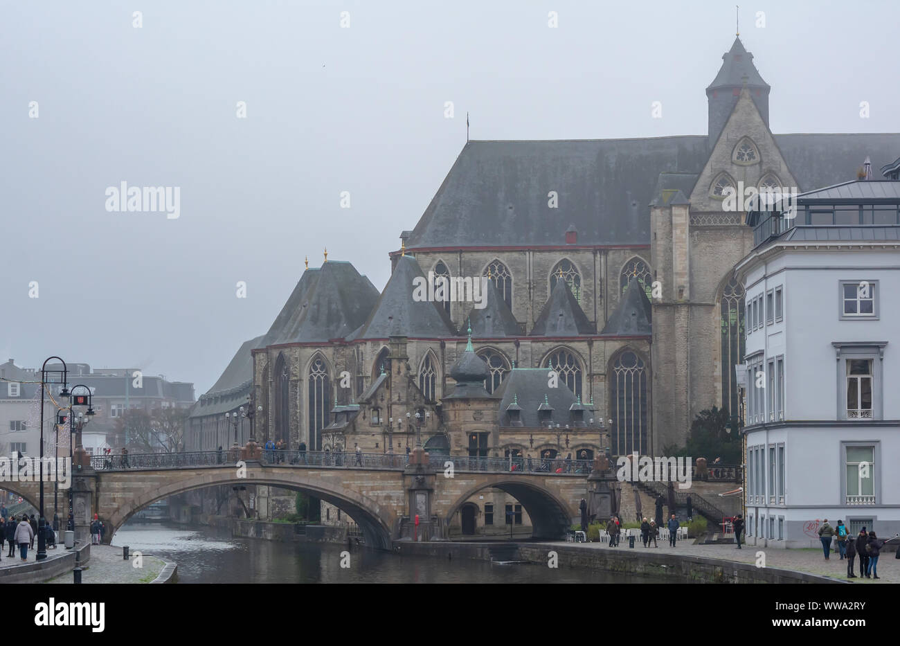 Tourists walking down the St. Michael's Bridge (Sint-Michielsbrug) near St. Michael's Church (Sint-Michielskerk) in foggy winter morning. Stock Photo