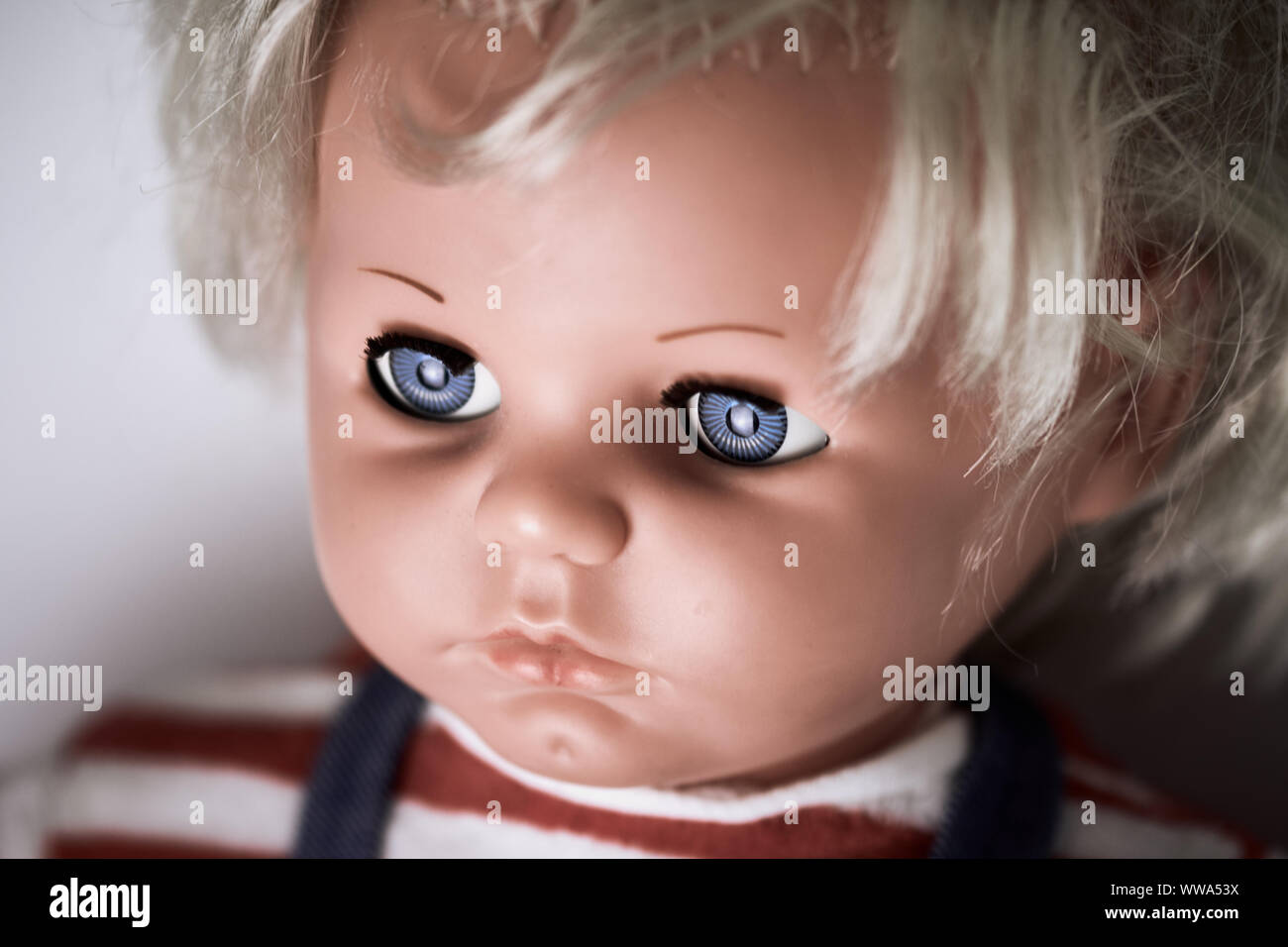 Creepy doll's head. A scary face of a blonde baby doll with blue eyes and a red white striped shirt Stock Photo