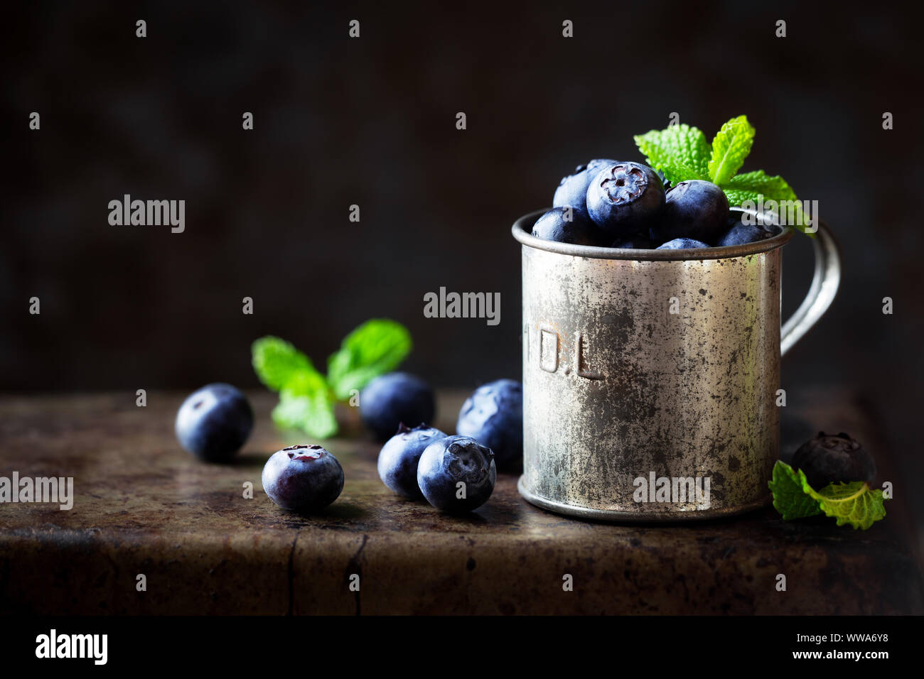 Fresh ripe garden blueberries in a vintage tin measuring cup against dark rustic background with copyspace for your text Stock Photo