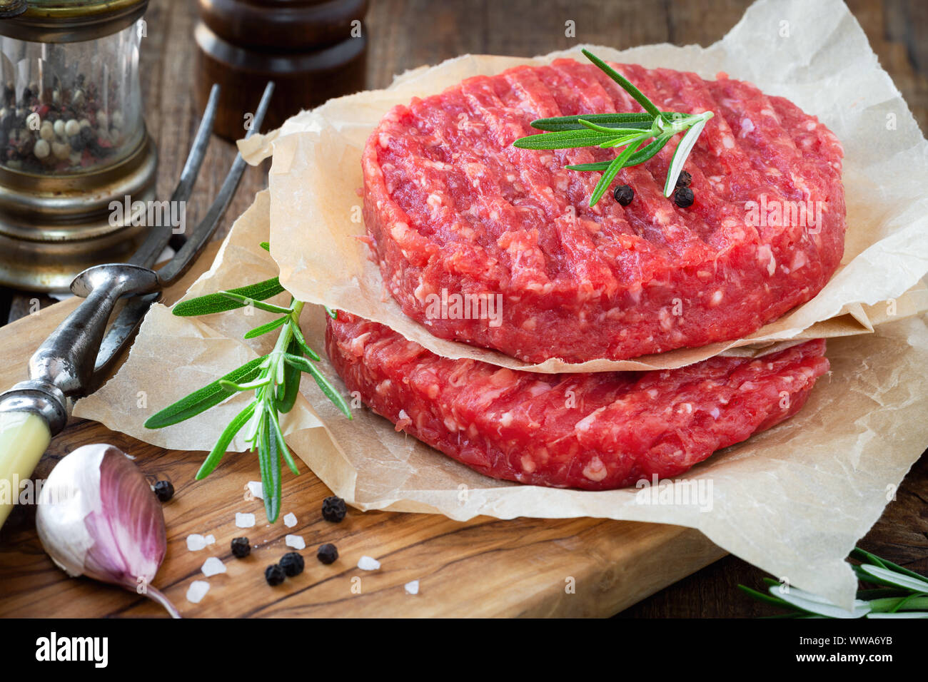 Raw mince meat beef burgers on a wooden cutting board with fresh rosemary, cloves of garlic