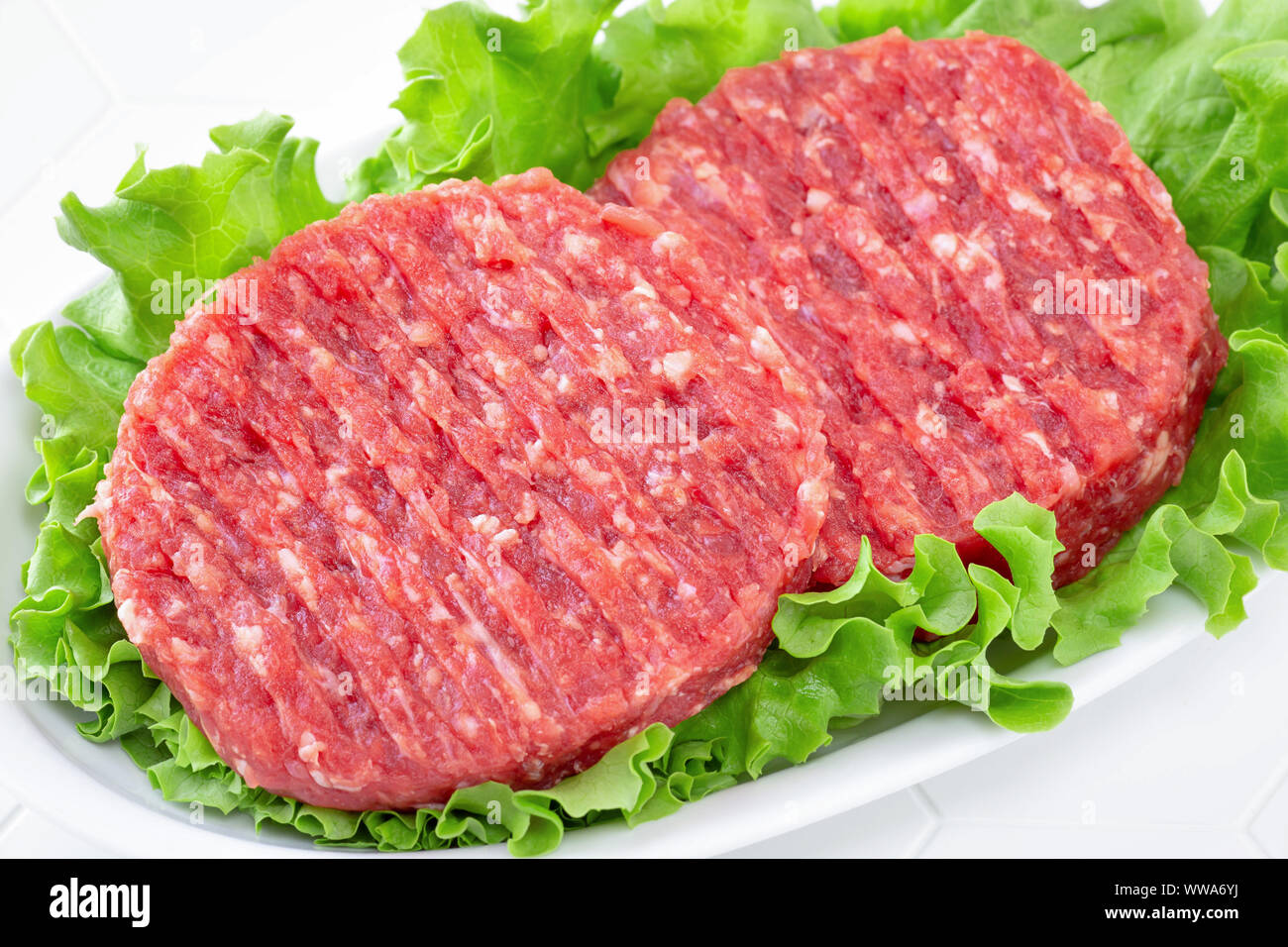 Raw mince meat beef burgers on a white plate with lettuce leaves Stock Photo