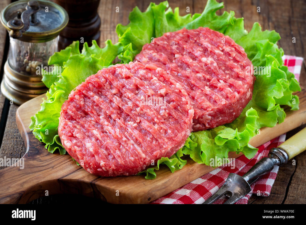 Raw mince meat beef burgers on a wooden cutting board with lettuce leaves Stock Photo