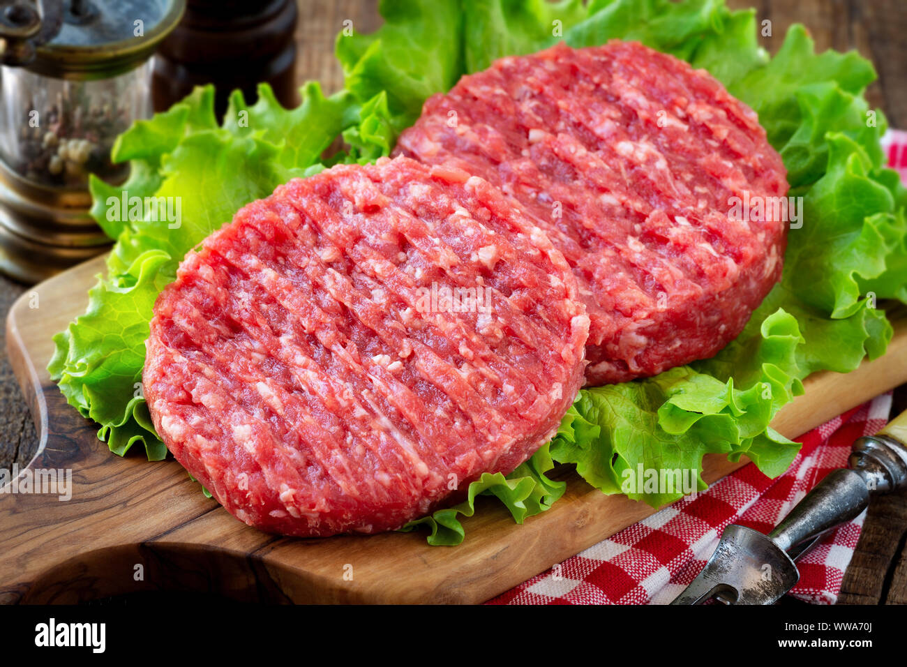 Raw mince meat beef burgers on a wooden cutting board with lettuce leaves Stock Photo