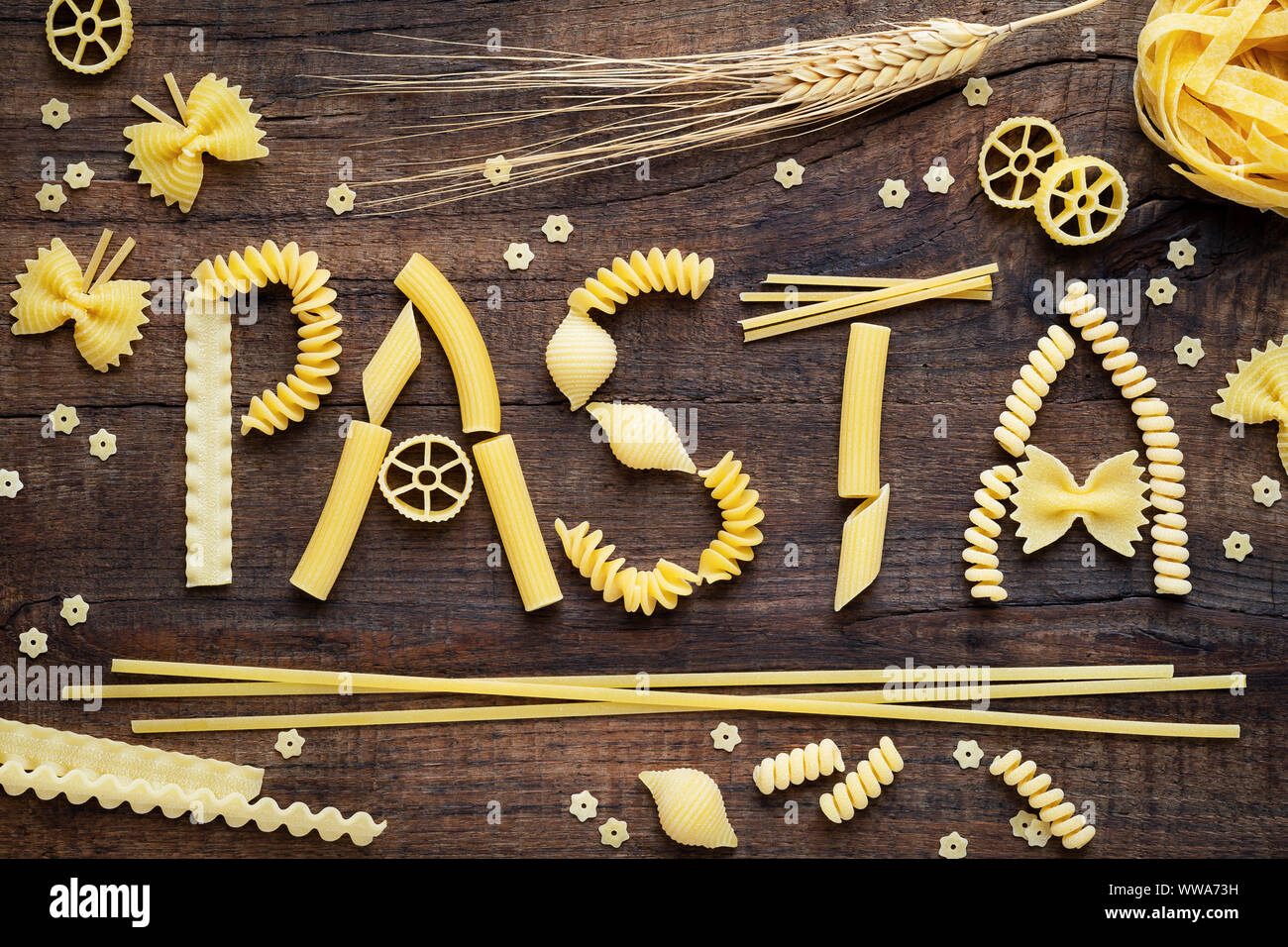 Variety of types and shapes of dry Italian pasta concept. Pasta word made of fusilli, spaghetti, penne, conchiglie, farfalle and ruote Stock Photo