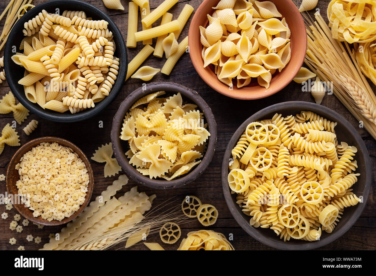 Variety of types and sshapes of dry Italian pasta in bowls against dark rustic wooden background Stock Photo