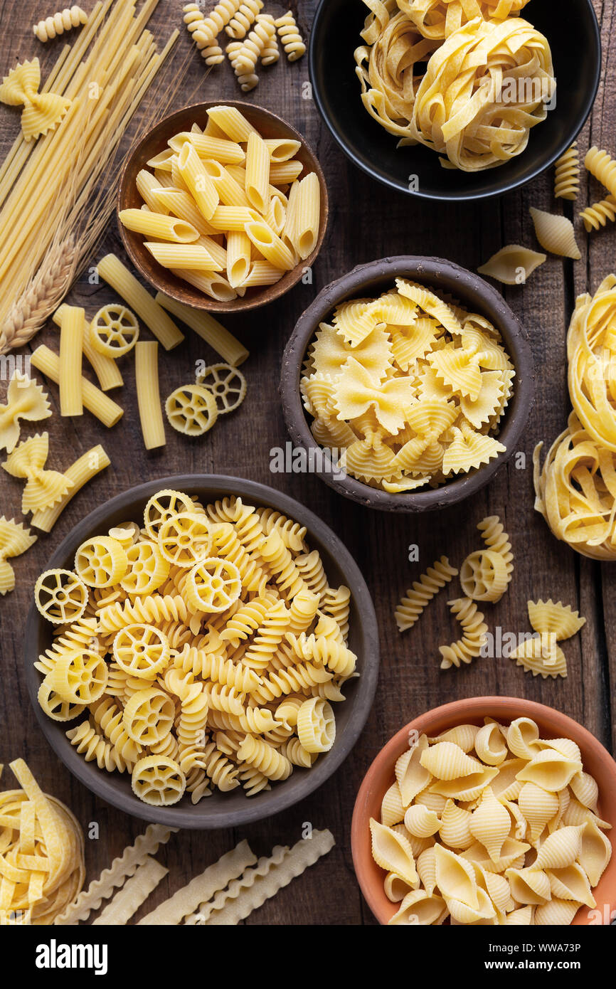 Variety of types and sshapes of dry Italian pasta in bowls against dark rustic wooden background Stock Photo