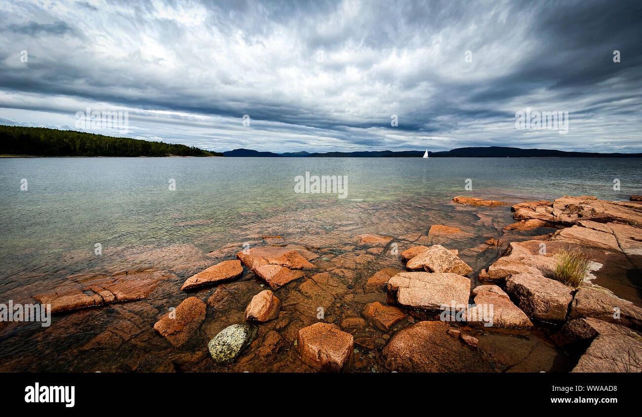 Lonely sail boat in archipelago. Dramatic sky over stony beach coast and shallow water. Storsand, High Coast in northern Sweden. Stock Photo