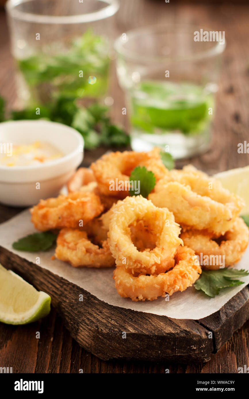 Fried calamari rings on wooden cutting board with lemon and parsley Stock Photo