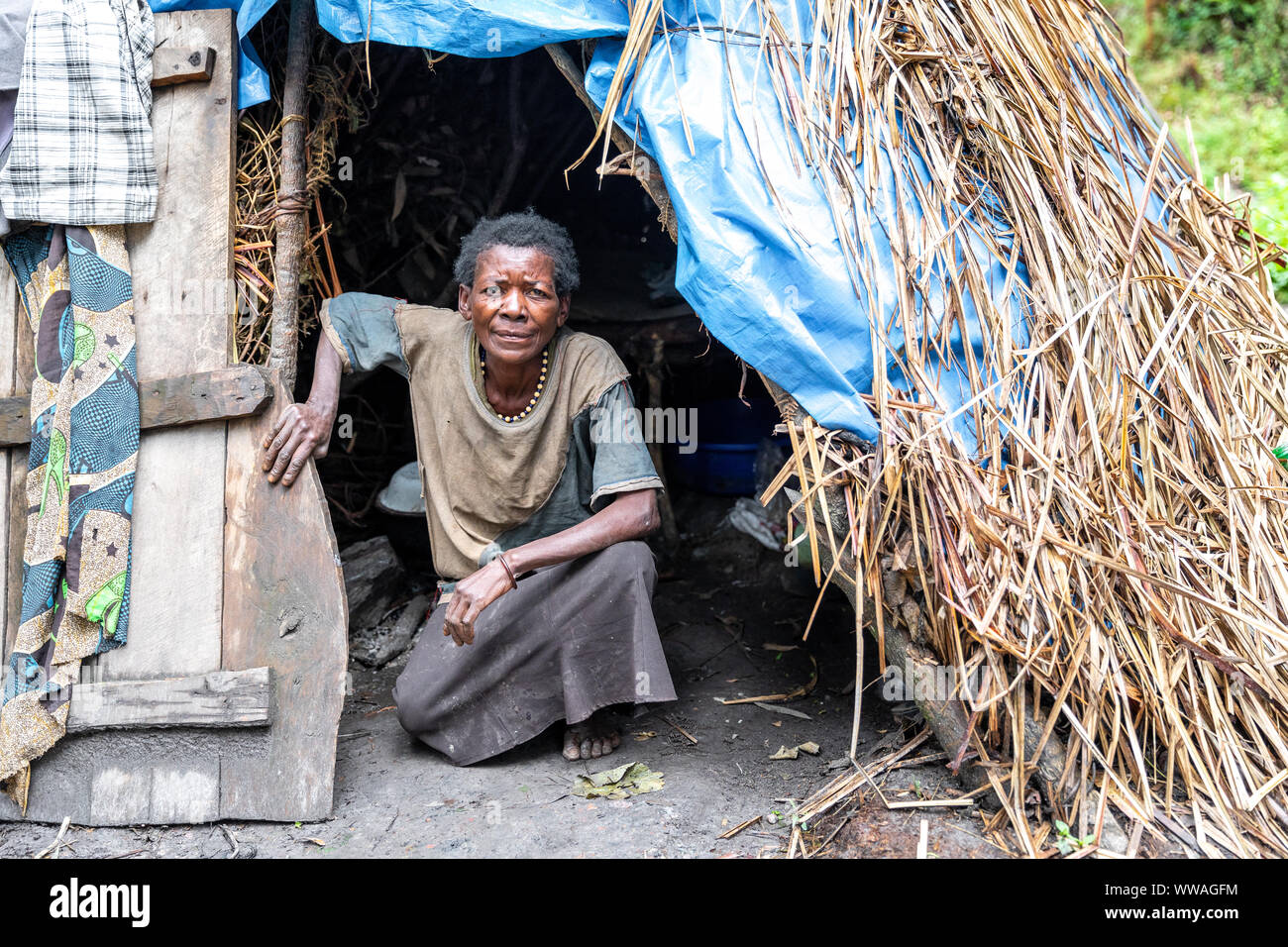 Portrait of pygmy tribeswoman crouching in front of primitive hut, Uganda Stock Photo