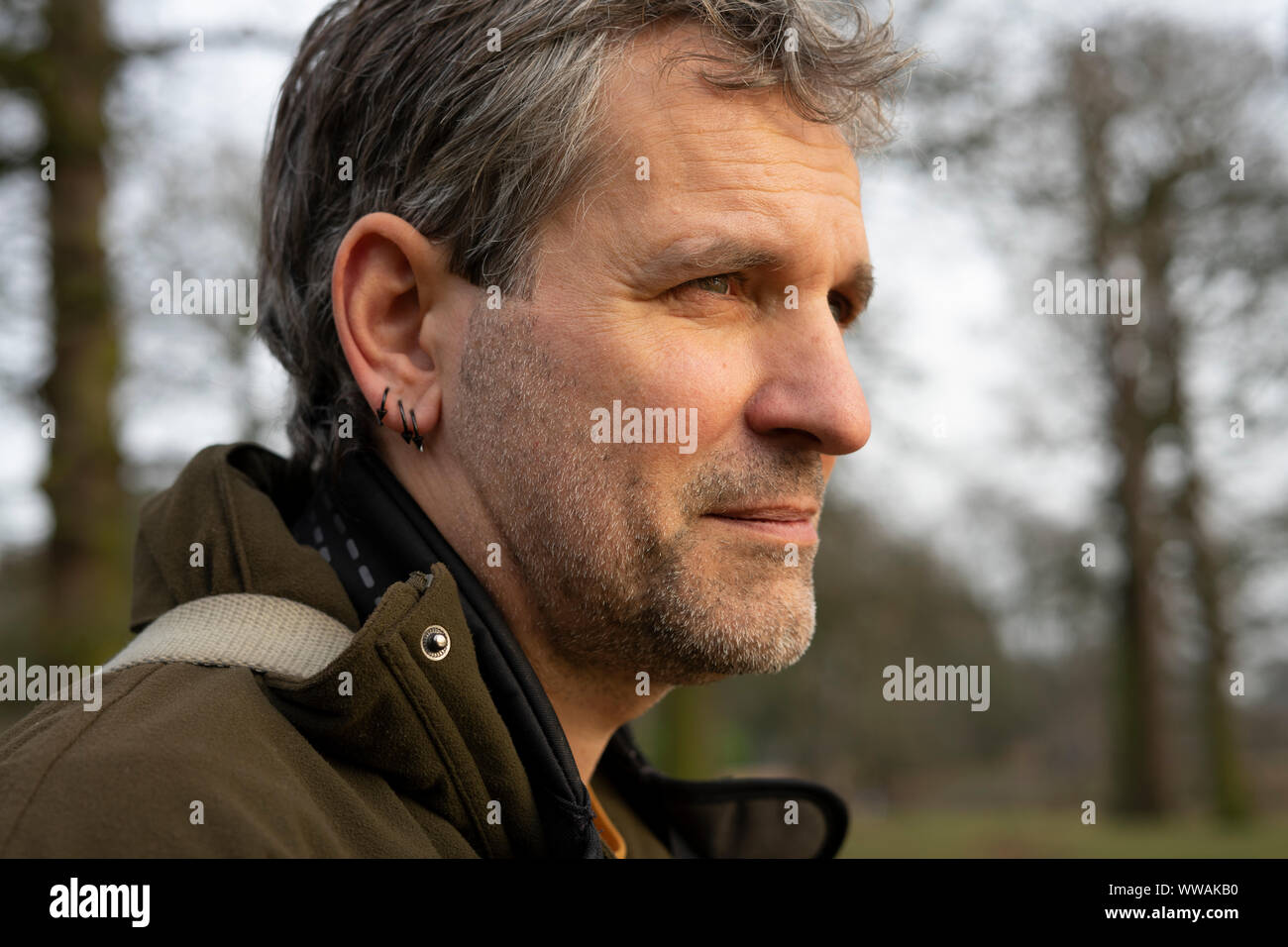 Close-up portrait of a man in his 50's, grey hair wearing a coat and carrying a camera Stock Photo